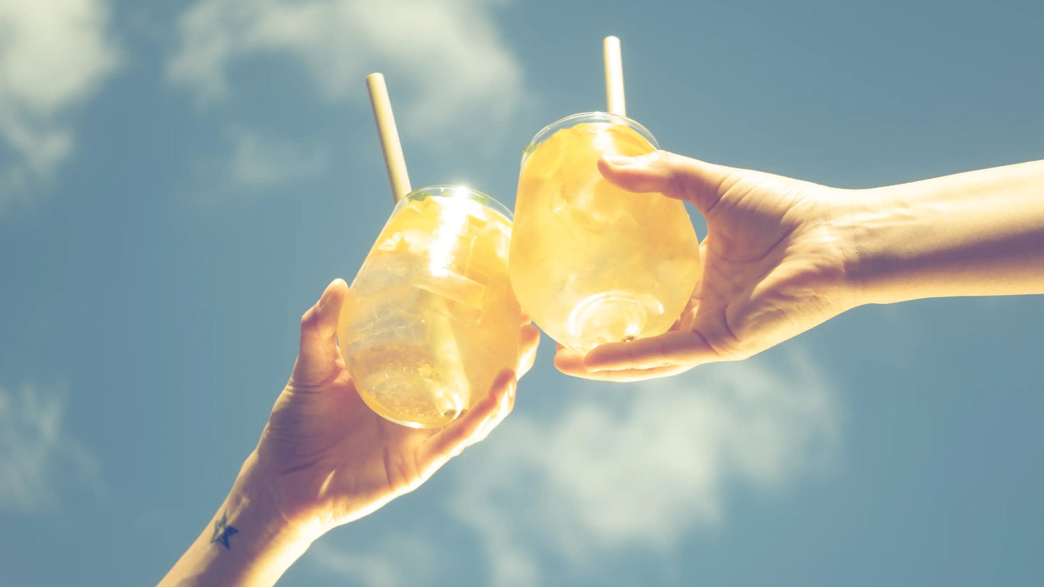 Két kéz aranyló spritz koktéllal koccint a kék ég alatt, nyári hangulatban, Cseles italból készítve.