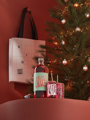 Karácsonyi ajándékcsomag: egy literes meggyes, szefűszeges, fahéjas Cseles likőr üveg, két egyedi Cseles koktélpohár, fém kiöntő és vászontáska ünnepi háttérrel – tökéletes koktél alap, likőr ajándék, karácsonyi ajándék és karácsonyi csomag.