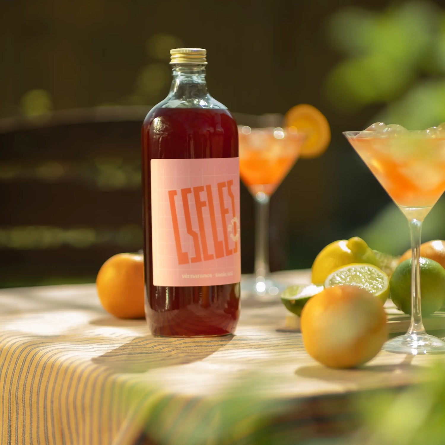Cseles üveg és friss citrusos spritz koktélok egy napfényes asztalon, nyári kerti hangulatban.