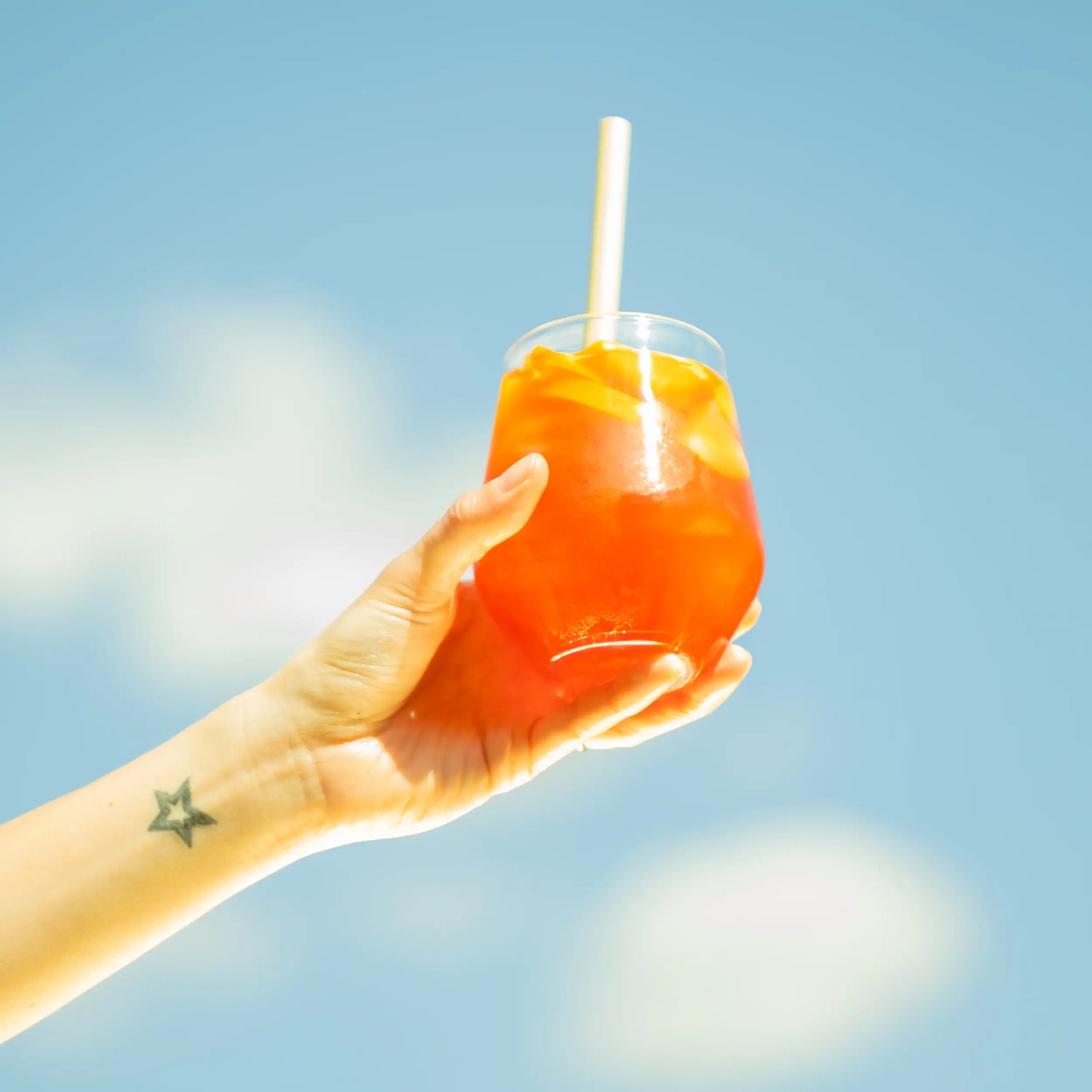 Cseles spritz koktél kézben tartva a kék ég alatt, napsütéses nyári hangulatban.